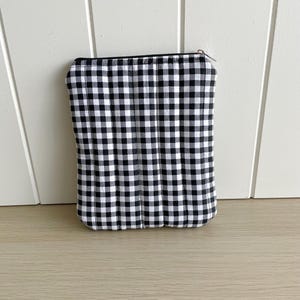 May include: Black and white gingham zippered pouch. The pouch is made of fabric and has a quilted look.