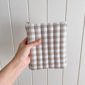Peut inclure: Une pochette zippée matelassée en vichy beige et blanc. La pochette est faite d'un tissu matelassé doux et possède une fermeture à glissière.