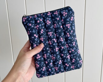 May include: A quilted zippered pouch with a floral pattern in shades of pink and blue on a dark navy background.