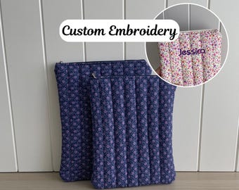 May include: Two zippered pouches with floral patterns. The larger pouch is navy blue with a white floral pattern. The smaller pouch is white with a pink and purple floral pattern. The smaller pouch has the name "Jesssica" embroidered on it in purple thread.  Custom Embroidery.