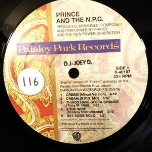May include: A black vinyl record label featuring a cream and gold paisley background. Text includes Prince and the N.P.G., Paisley Park Records, and a tracklist for the album Diamonds and Pearls. A white circular sticker with the number 116 is present.