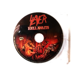 May include: A compact disc with the album title "Hell Awaits" by the band Slayer. The disc has a dark red and black background with a graphic illustration. The band's name is in red, stylized lettering.