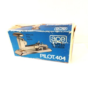 May include: A vintage Ace Pilot 404 stapler-tacker in its original box. The box is blue with white text and a silver stapler illustration. The stapler is silver and appears to be made of metal.