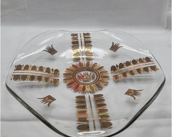 May include: A clear glass serving dish with a gold and brown geometric design. The design features a crown and a repeating pattern of leaves. The dish is marked "Ginger" and "Evans".