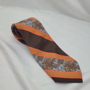 May include: A brown and orange striped tie with a paisley pattern. The tie features alternating wide brown stripes and orange stripes. The paisley pattern is in shades of brown, gray, and white.