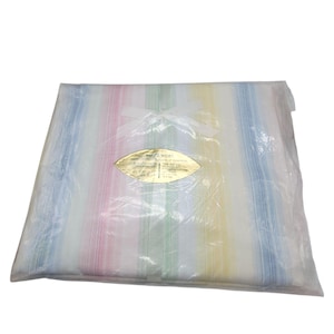 May include: A folded, striped textile in a clear plastic bag. The stripes are vertical and in pastel colors: pink, yellow, green, and blue. A white ribbon is tied at the top. A gold-colored label is visible on the front.