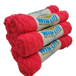 May include: A stack of bright red yarn skeins. Each skein is wrapped with a label that reads "WIN-LITE" in blue and white. The yarn is labeled as machine or hand washable. The yarn is made of 97% Acrylic and 3% Nylon.