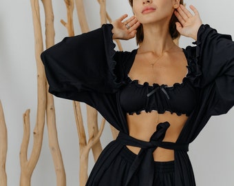 May include: A black satin robe with a ruffled neckline and a matching bra. The robe has a tie at the waist and a slit up the front.
