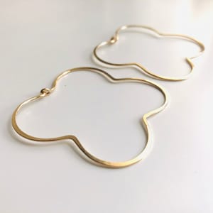 May include: A pair of gold-toned, open-hoop earrings with a unique, asymmetrical, cloud-like shape.