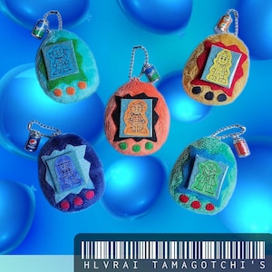 May include: A collection of plush Tamagotchi keychains in various colors, including teal, orange, yellow, and blue. Each keychain features a small screen with a character design and a miniature soda can charm. The text "HLVRAI TAMAGOTCHI'S" is at the bottom.