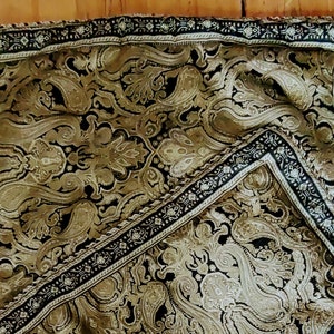 May include: A black and gold throw pillow with a damask pattern and a decorative border.