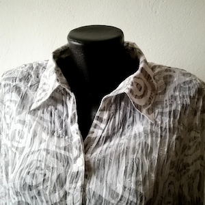 Puede incluir: Una camisa blanca de botones con un estampado abstracto gris. La camisa tiene cuello y mangas largas.