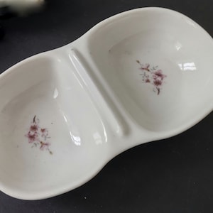 Könnte beinhalten: Eine weiße, geteilte Keramikschale mit zwei kleinen Schalen. Jede Schale hat ein Blumenmuster mit rosa Blüten.