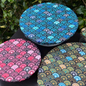 Peut inclure: Quatre couvercles alimentaires réutilisables de différentes tailles avec un motif géométrique d'écailles superposées dans des tons de bleu, vert, rose et noir.