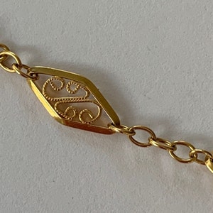 Puede incluir: Un collar de cadena de oro con un colgante en forma de diamante con un delicado diseño de filigrana.