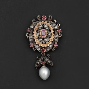 Può includere: Un ciondolo in argento e oro con una goccia di perla. Il ciondolo è decorato con un rubino centrale circondato da diamanti e piccoli rubini.