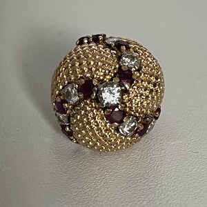 Op de afbeelding: Een gouden ring met een getextureerd oppervlak en een cluster van rode robijnen en witte diamanten.
