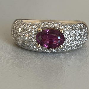 May include: A gold ring with a large oval-shaped purple gemstone surrounded by smaller white gemstones.