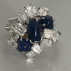 Può includere: Un anello d'argento con un gruppo di zaffiri blu e diamanti. Gli zaffiri sono incastonati a griffe e i diamanti sono incastonati a pavé.