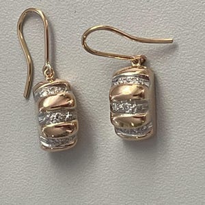 May include: A pair of gold-tone earrings with a barrel-shaped design. The earrings feature alternating bands of gold and silver, with the silver bands encrusted with small, sparkling stones. The hooks are a simple, curved design.
