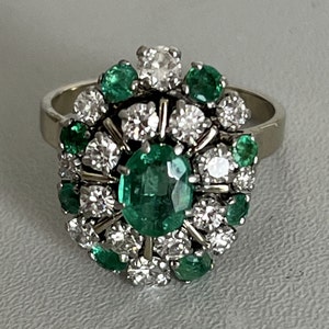Può includere: Un anello d'argento con un grande smeraldo circondato da smeraldi e diamanti più piccoli.
