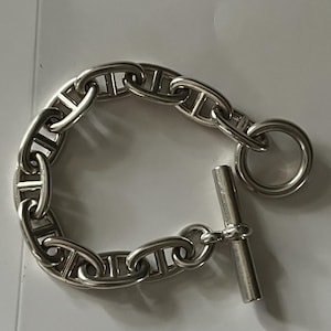 May include: A silver chain bracelet with a toggle clasp. The chain is made of interlocking links in a nautical design.