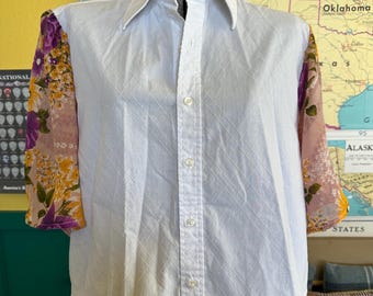 May include: White button-down shirt with floral patterned sleeves in shades of purple, yellow, and pink. The shirt has a classic collar and a subtle diamond pattern on the front. A vintage-inspired garment.
