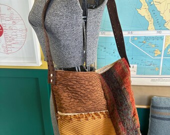 May include: A shoulder bag with a brown leather strap and a mixed-material body. The bag features sections of textured brown fabric, a golden-yellow woven material, and a section of colorful, striped fabric. The strap is attached with a silver buckle.