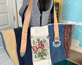 May include: A patchwork tote bag with denim, beige, and patterned fabric panels. Features a floral needlepoint pocket, leather straps, and turquoise-accented metal hardware. The bag is displayed on a mannequin.