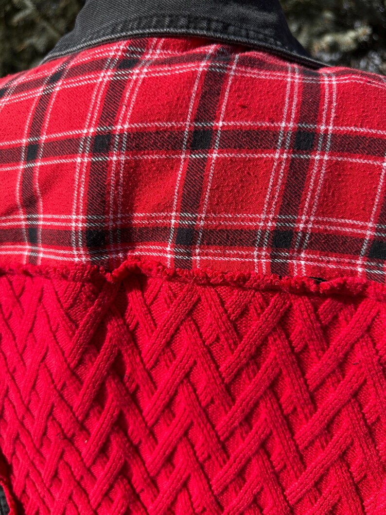 Puede incluir: Una camisa de franela a cuadros rojos y negros con cuello de mezclilla negro. La parte inferior de la espalda de la camisa presenta un dise&ntilde;o de punto de cable rojo texturizado. La camisa es una mezcla de texturas y patrones.