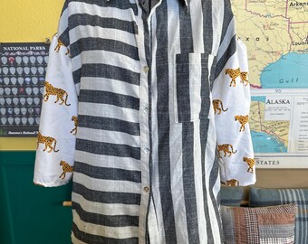 May include: A button-down shirt with a unique design. One side features vertical black and white stripes, while the other has white sleeves with leopard print. The shirt is displayed on a mannequin.