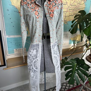 May include: A light blue long-sleeved shirt with a floral print and a white lace overlay. The shirt has a pointed collar and a button-up front.