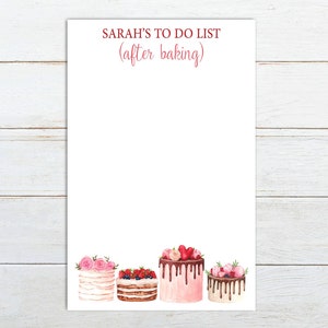 May include: A white notepad with the text "SARAH'S TO DO LIST (after baking)" at the top. The bottom of the notepad features a row of five decorated cakes with pink frosting, chocolate, and fruit toppings.