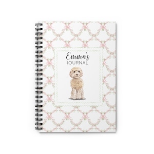 May include: Spiral-bound journal with a white cover featuring a repeating pattern of pink bows and floral elements. The center has a square frame with the text "Emma's JOURNAL" and a watercolor illustration of a fluffy, tan dog.