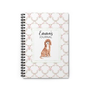 May include: Spiral-bound notebook with a watercolor illustration of a Cavalier King Charles Spaniel. The cover features the text "Emma's JOURNAL" within a decorative frame, set against a white background with a pink floral pattern.