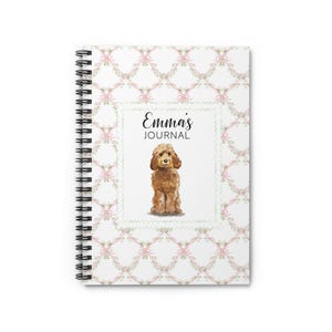 May include: Spiral-bound journal with a white cover featuring a repeating pattern of pink bows and green leaves. The center has a watercolor illustration of a brown dog and the text "Emma's JOURNAL".