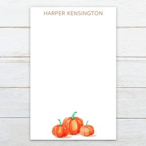May include: A white notepad with the text "HARPER KENSINGTON" at the top. The notepad has a watercolor illustration of three orange pumpkins at the bottom.