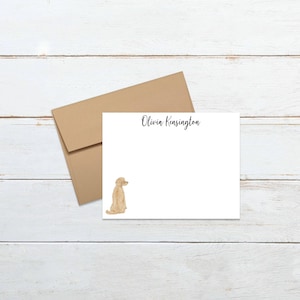 May include: A white card with a light brown dog illustration and the text "Olivia Kensington" at the top. The card is on a light brown wooden surface.