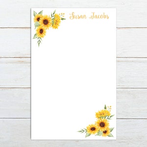 May include: A white notepad with a sunflower design on the top and bottom corners. The notepad has the name "Susan Jacobs" printed in gold lettering at the top.