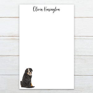 May include: White stationery with the name "Olivia Kensington" in black script at the top. A watercolor illustration of a Bernese Mountain Dog is at the bottom left. The dog is black, white, and brown.