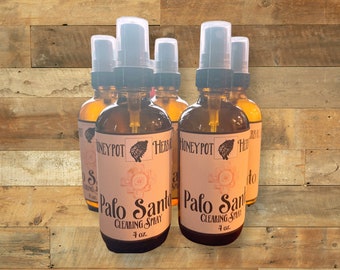 Peut inclure: Plusieurs flacons en verre ambré de Palo Santo Clearing Spray, chacun avec un bouchon pulvérisateur noir et une étiquette avec le texte "Palo Santo Clearing Spray 4 oz." Les flacons sont disposés sur une surface en bois.