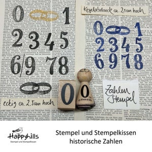 Op de afbeelding: Een verzameling vintage rubberen stempels met de cijfers 0 tot en met 9. De stempels zijn in verschillende kleuren, waaronder zwart, blauw en rood. De stempels zijn in willekeurige volgorde gerangschikt. De tekst "Kegelabdruck ca. 2.1cm hoch" is zichtbaar in de afbeelding. De tekst "Zahlen Hempel" is ook zichtbaar in de afbeelding. De afbeelding is geplaatst tegen een achtergrond van een pagina uit een boek.