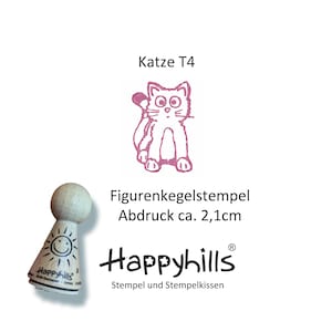 May include: A pink rubber stamp with a cartoon cat design. The stamp is mounted on a wooden handle with a smiley face and the text "Happyhills" on it. The text "Katze T4" and "Figurenkegelstempel Abdruck ca. 2,1cm" is also visible on the image.