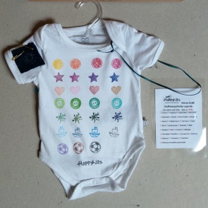 May include: White baby onesie with a colorful pattern of stamped images, including lemons, stars, hearts, buttons, paint splatters, paper boats, and soccer balls. The onesie has the text "Happyhills" printed on the bottom.