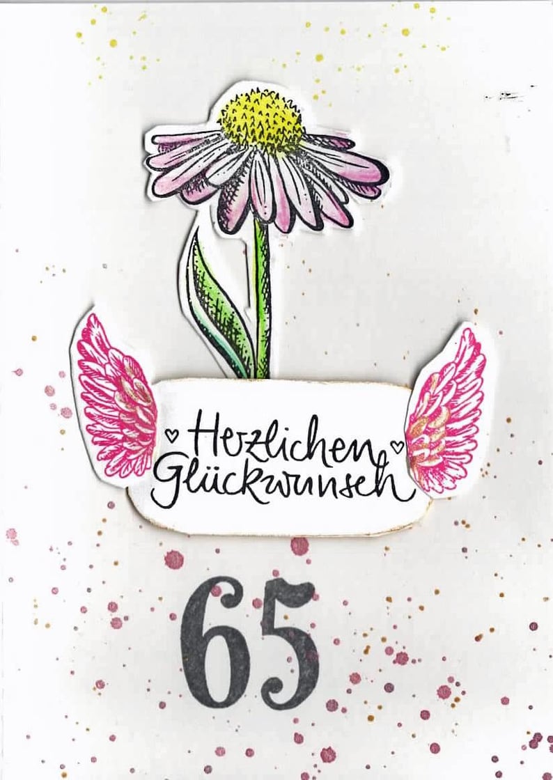 Op de afbeelding: Een witte kaart met roze en gouden glitteraccenten. Een roze bloem met een gele kern bevindt zich bovenaan de kaart. Onder de bloem bevinden zich twee roze vleugels met gouden glitteraccenten. De tekst "Herzlichen Gl&uuml;ckwunsch" staat op de kaart. Het nummer 65 staat onderaan de kaart in het zwart.
