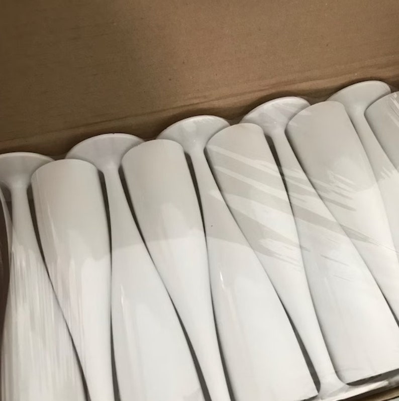 May include: A box of white plastic champagne flutes. The flutes are arranged in rows and are wrapped in plastic.