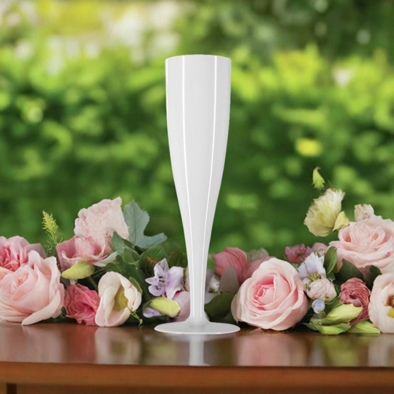 May include: A white plastic champagne flute sits on a table with pink flowers.