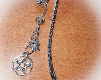 Puede incluir: Marcapáginas de plata con un amuleto de pentagrama, un amuleto de escoba y un diseño decorativo en el marcapáginas.