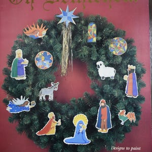 May include: A Christmas wreath with various nativity scene cutouts. The wreath is adorned with a star, a stained glass window, a sheep, and figures of the nativity scene. The text "Oh Bethlehem" is at the top, and "Designs to paint on watercolor paper for ornaments and jewelry" is at the bottom.