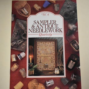 May include: A copy of Sampler & Antique Needlework Quarterly, Vol. 4, featuring a framed sampler with a candle and various antique sewing tools. The cover is surrounded by thimbles and other needlework accessories on a red background.